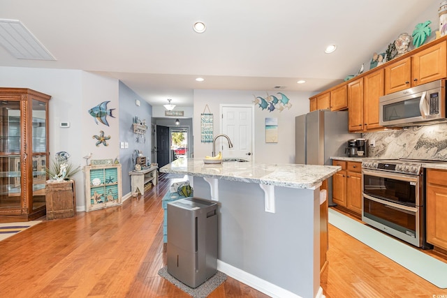 kitchen with appliances with stainless steel finishes, sink, a kitchen bar, light stone counters, and an island with sink