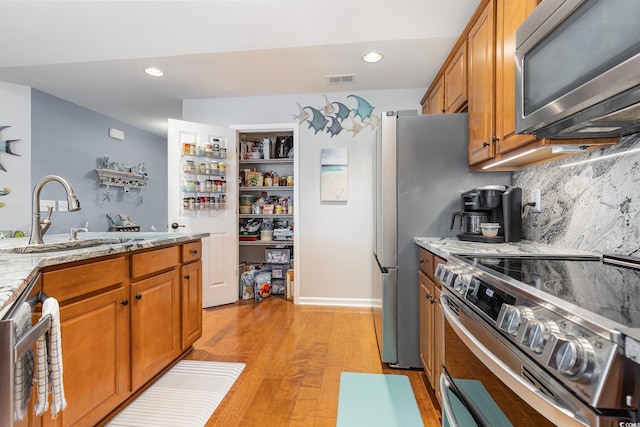 kitchen with appliances with stainless steel finishes, sink, light stone counters, and light hardwood / wood-style flooring