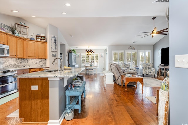 kitchen with stainless steel appliances, light stone countertops, lofted ceiling, sink, and a kitchen island with sink