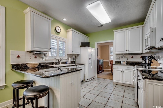 kitchen with white appliances, dark stone counters, light tile patterned floors, sink, and white cabinetry