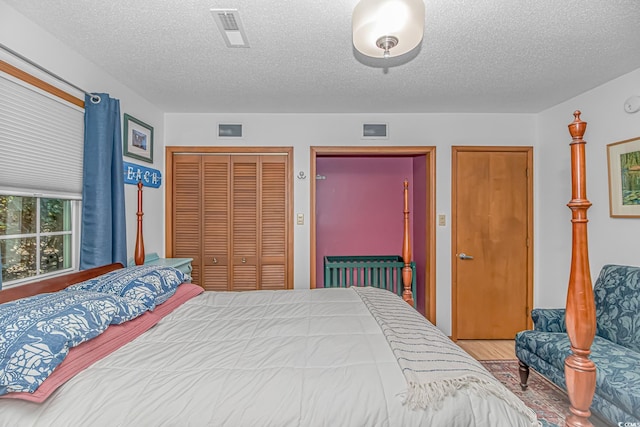 bedroom with a closet, visible vents, a textured ceiling, and wood finished floors