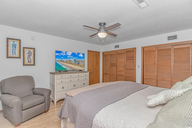 bedroom with a textured ceiling, light wood-style flooring, two closets, and visible vents