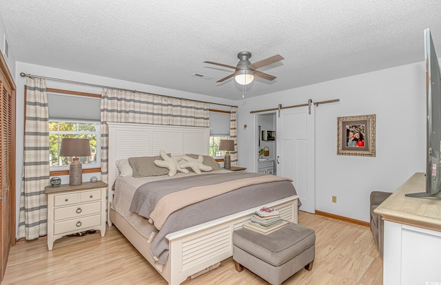 bedroom featuring light wood finished floors, visible vents, a barn door, ceiling fan, and a textured ceiling