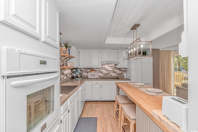 kitchen featuring under cabinet range hood, white cabinetry, decorative light fixtures, and oven