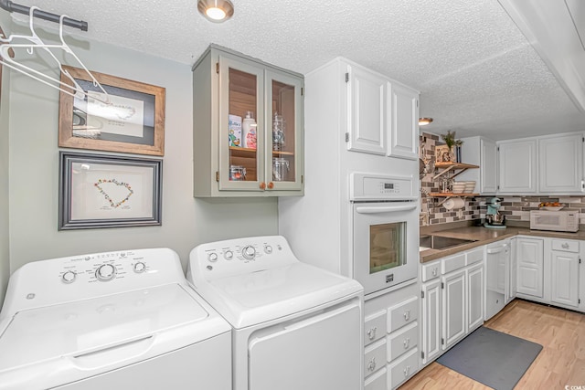 laundry room with light wood-style floors, washing machine and dryer, cabinet space, and a textured ceiling