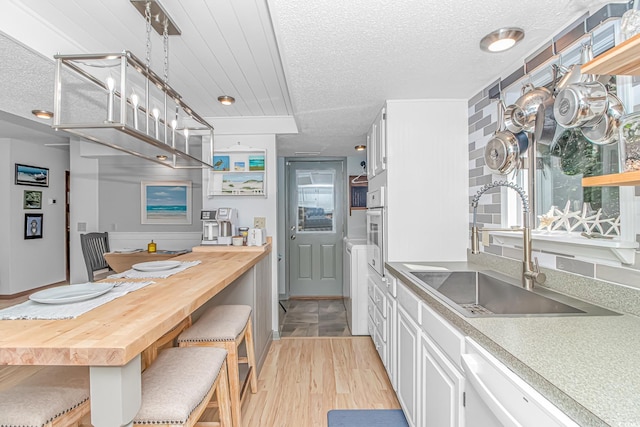 kitchen with a textured ceiling, white appliances, a sink, white cabinetry, and hanging light fixtures