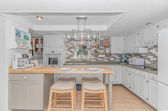 kitchen featuring white cabinetry, wood counters, white appliances, under cabinet range hood, and a kitchen bar