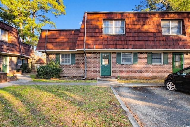 view of property with mansard roof, a front lawn, and brick siding