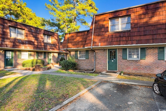 view of front of home with a front yard, brick siding, and mansard roof