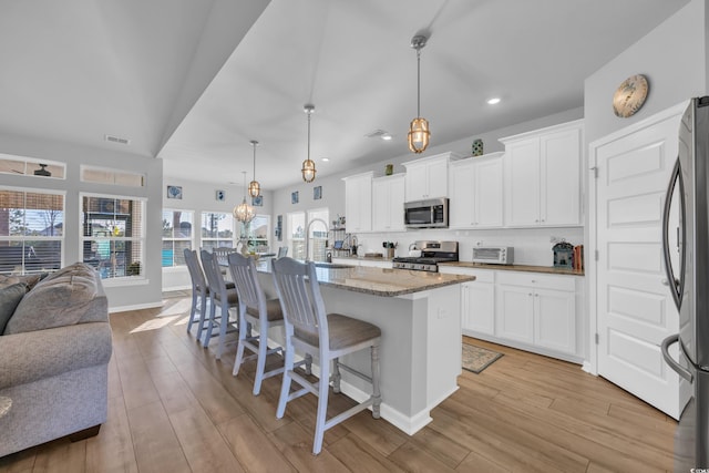 kitchen with visible vents, light stone countertops, open floor plan, light wood-type flooring, and stainless steel appliances