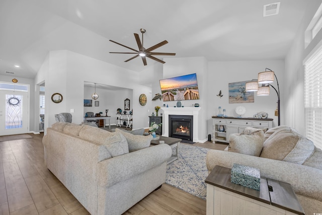 living room featuring vaulted ceiling, a glass covered fireplace, visible vents, and wood finished floors