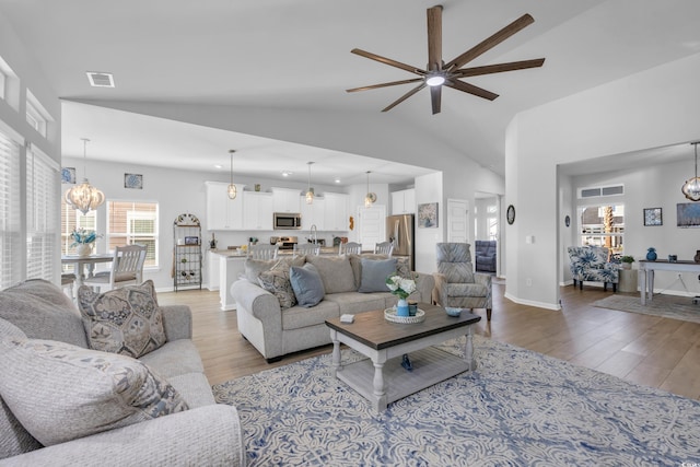 living room with visible vents, baseboards, lofted ceiling, ceiling fan with notable chandelier, and wood finished floors