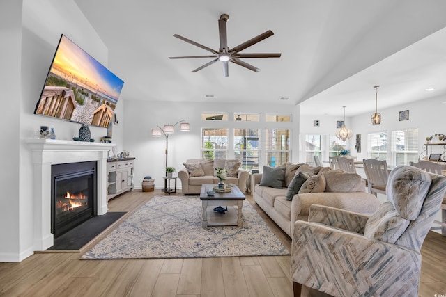 living room featuring a glass covered fireplace, vaulted ceiling, wood finished floors, and baseboards