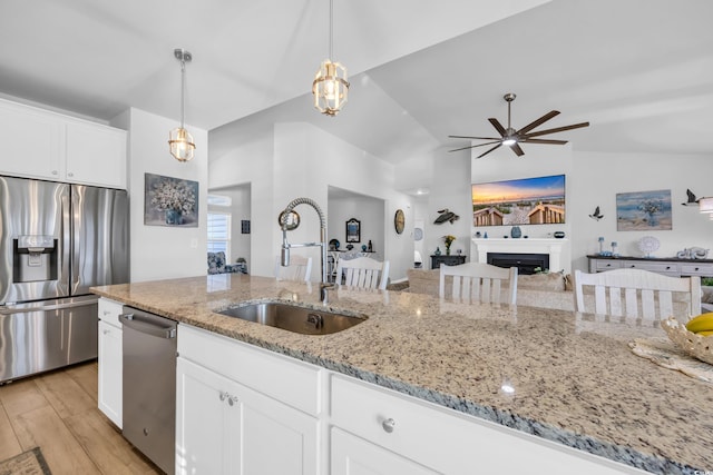 kitchen featuring light stone counters, appliances with stainless steel finishes, a fireplace, light wood-style floors, and a sink