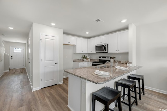 kitchen featuring appliances with stainless steel finishes, a kitchen breakfast bar, a peninsula, light wood-type flooring, and white cabinetry