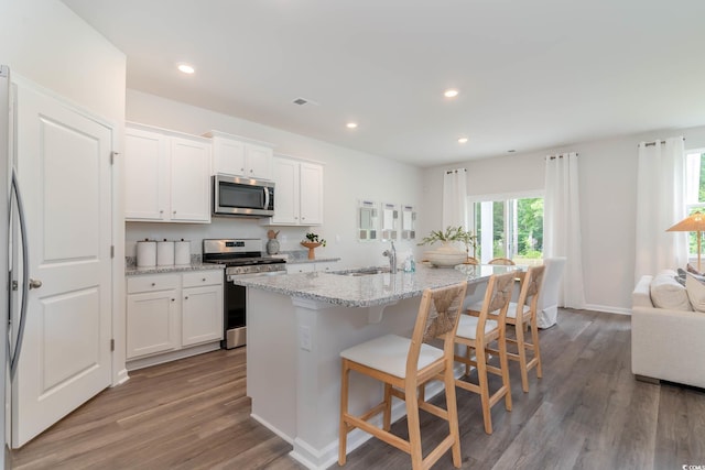 kitchen featuring light stone counters, a kitchen island with sink, light wood-style flooring, white cabinetry, and appliances with stainless steel finishes