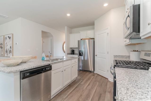 kitchen with a sink, light wood-style floors, white cabinets, appliances with stainless steel finishes, and a center island with sink