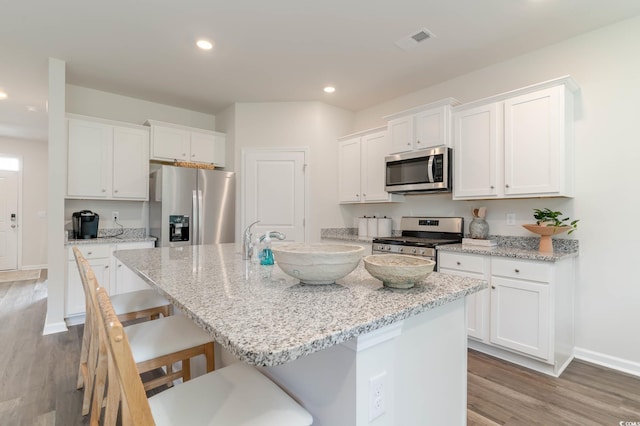 kitchen featuring visible vents, stainless steel appliances, a center island with sink, and white cabinets