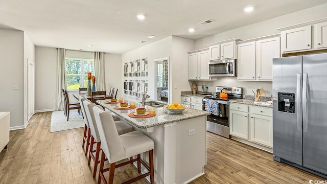 kitchen featuring a kitchen island with sink, light wood finished floors, a sink, and appliances with stainless steel finishes