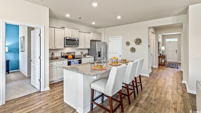 kitchen with a sink, appliances with stainless steel finishes, a kitchen breakfast bar, dark wood finished floors, and a center island with sink