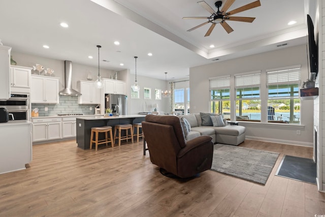 living room featuring ceiling fan, ornamental molding, light hardwood / wood-style floors, and a raised ceiling