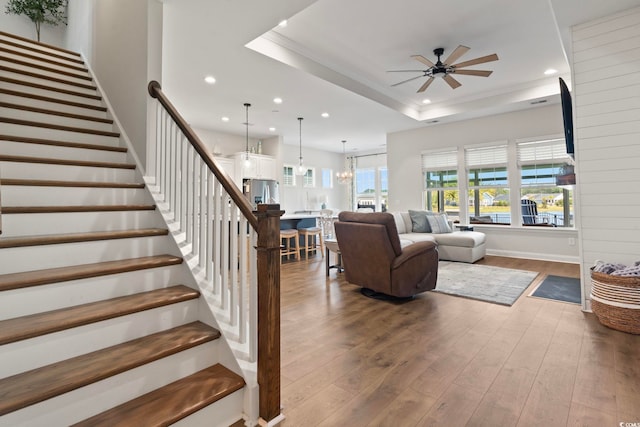 living room with ceiling fan with notable chandelier, wood-type flooring, and a raised ceiling