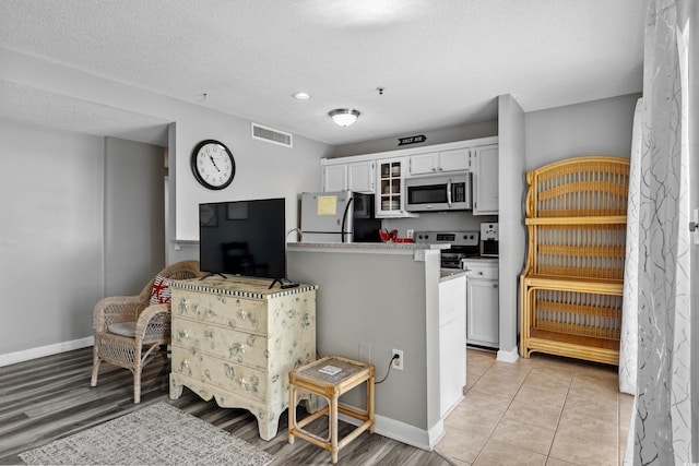 kitchen featuring appliances with stainless steel finishes, light tile patterned flooring, white cabinetry, a textured ceiling, and kitchen peninsula