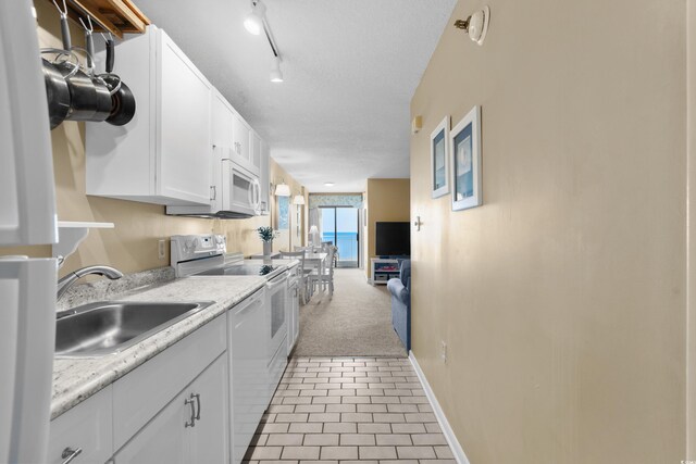 kitchen with sink, white appliances, light tile patterned floors, a textured ceiling, and white cabinets