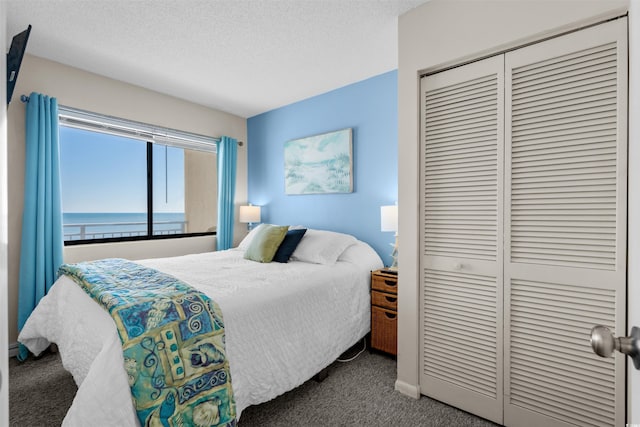 carpeted bedroom featuring a water view, a closet, and a textured ceiling