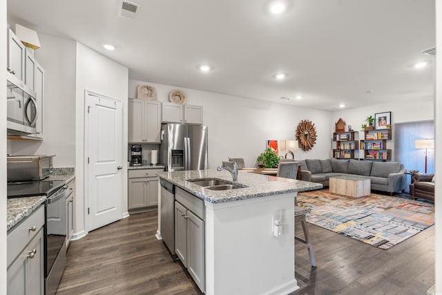 kitchen with an island with sink, appliances with stainless steel finishes, open floor plan, light stone countertops, and a sink