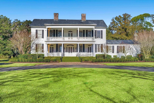 view of front of house with covered porch, a balcony, a chimney, and a front lawn