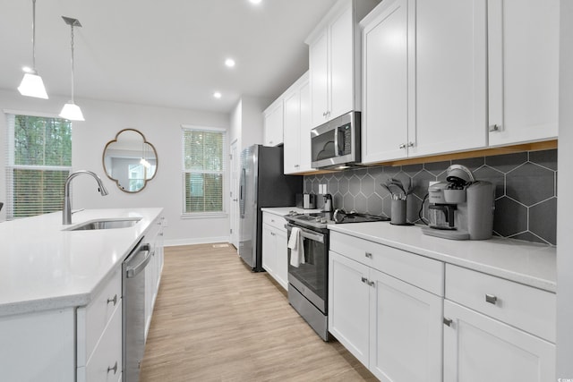 kitchen with appliances with stainless steel finishes, sink, decorative light fixtures, light hardwood / wood-style floors, and white cabinets