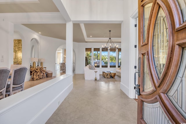 entryway with a raised ceiling, an inviting chandelier, crown molding, and light tile patterned flooring