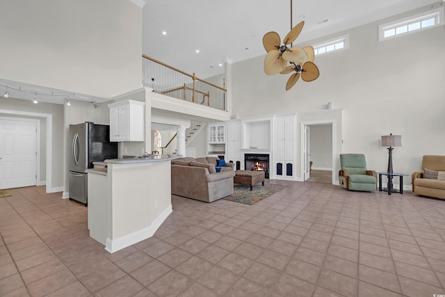 tiled living room with a towering ceiling, rail lighting, and ceiling fan