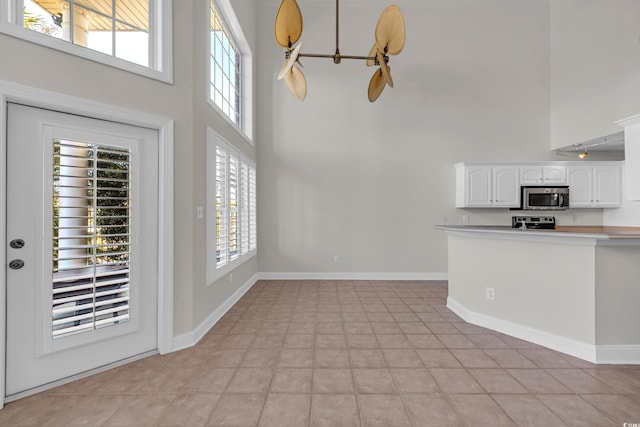 kitchen with appliances with stainless steel finishes, pendant lighting, a towering ceiling, kitchen peninsula, and white cabinets