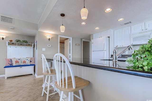 kitchen featuring white appliances, light tile patterned floors, white cabinets, a kitchen bar, and pendant lighting