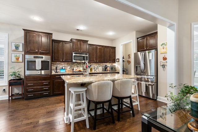 kitchen with a center island with sink, tasteful backsplash, a breakfast bar area, dark wood-type flooring, and stainless steel appliances