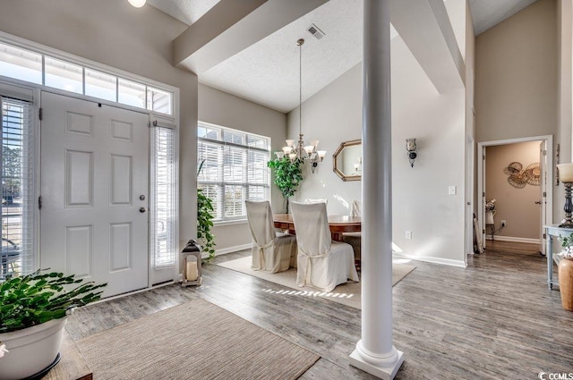 entrance foyer featuring high vaulted ceiling, light wood-type flooring, an inviting chandelier, and decorative columns