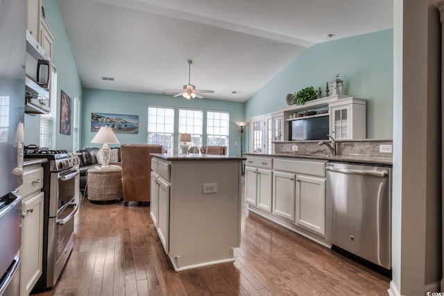 kitchen featuring stainless steel appliances, wood finished floors, a kitchen island, white cabinetry, and vaulted ceiling