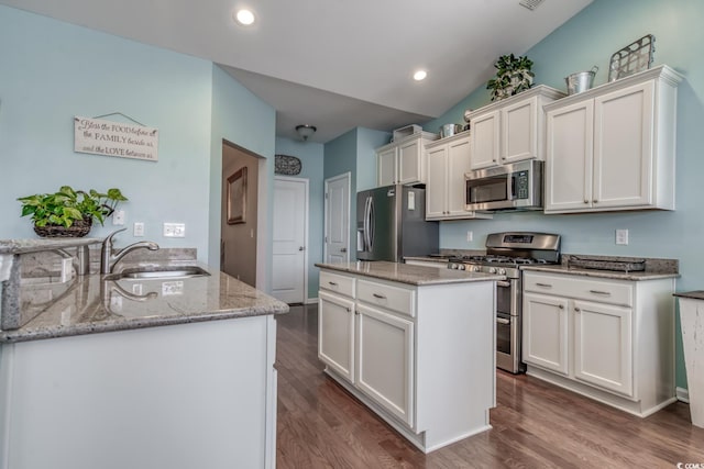 kitchen with light stone counters, stainless steel appliances, a peninsula, a sink, and white cabinetry