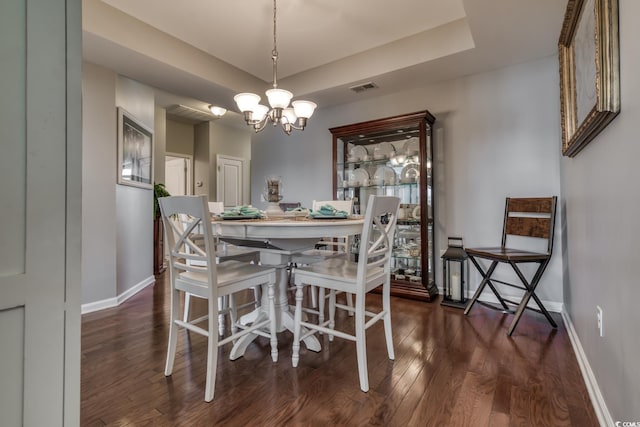 dining space featuring baseboards, visible vents, a tray ceiling, and dark wood-type flooring