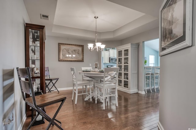 dining space with baseboards, visible vents, dark wood-style flooring, a tray ceiling, and a chandelier