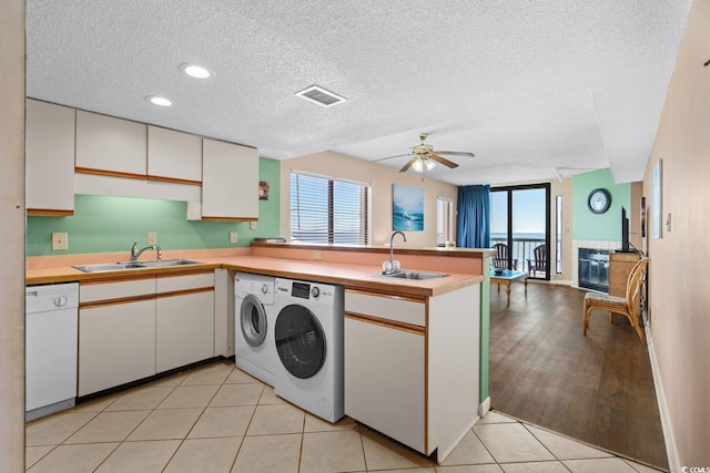 kitchen with dishwasher, sink, washer and dryer, white cabinetry, and kitchen peninsula