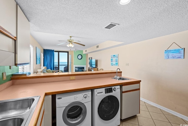 washroom with a textured ceiling, washing machine and dryer, light tile patterned flooring, ceiling fan, and sink