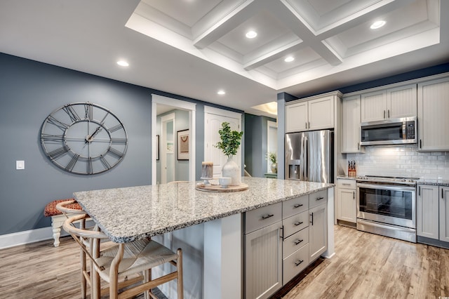 kitchen featuring a breakfast bar, backsplash, light stone counters, a center island, and stainless steel appliances