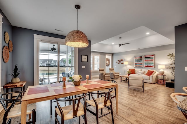 dining space with ceiling fan, light wood-type flooring, and a raised ceiling