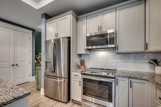 kitchen with appliances with stainless steel finishes, light hardwood / wood-style flooring, light stone countertops, and decorative backsplash