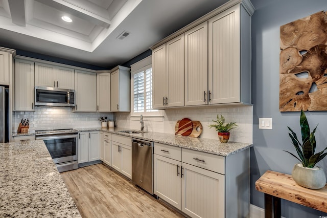 kitchen featuring sink, backsplash, light stone counters, light hardwood / wood-style floors, and stainless steel appliances