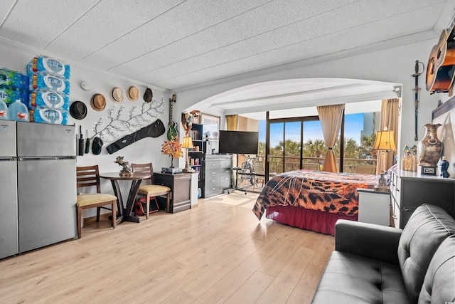 bedroom with arched walkways, freestanding refrigerator, crown molding, and light wood-style flooring