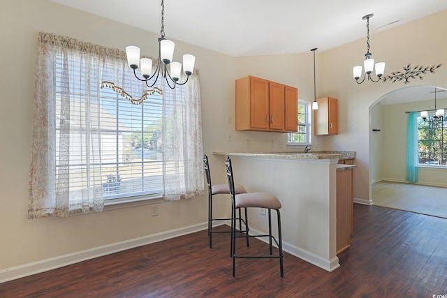 kitchen with a kitchen bar, an inviting chandelier, vaulted ceiling, dark hardwood / wood-style floors, and kitchen peninsula